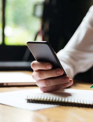 Cropped photo of young man in white shirt holding smartphone, while resting after paperwork